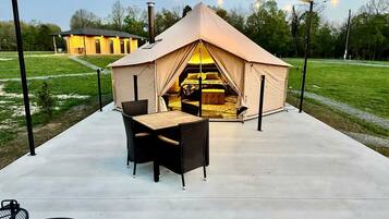 Een tent met een bed aan de binnenkant, een tafel en stoelen buiten.