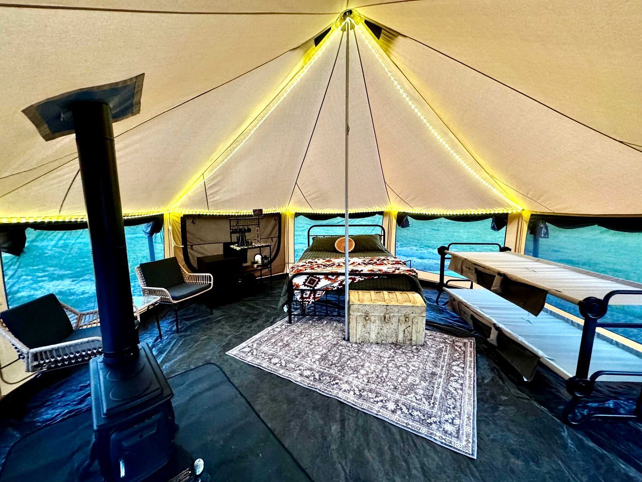 Een tentaccommodatie met een centraal bed, zithoek en een kooktoestel.