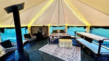 Een tentaccommodatie met een centraal bed, zithoek en een kooktoestel.