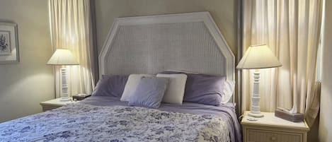 A bedroom with a bed, two bedside tables, a headboard, and curtains.