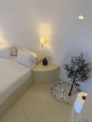 Une chambre à coucher avec un lit, une table de chevet avec une lampe, un vase décoratif et un petit arbre artificiel.