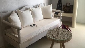 Un divano bianco con numerosi cuscini, un tavolino con piano in mosaico e un appendiabiti.