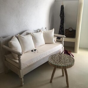 Ein weißes Sofa mit vielen Kissen, ein runder Tisch mit Mosaikplatte und ein an der Wand hängender Kleiderhaken.