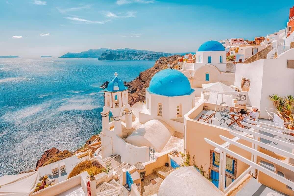 Ein Küstengebäude mit weißen Wänden und blauen Kuppeln mit Blick auf ein Gewässer.