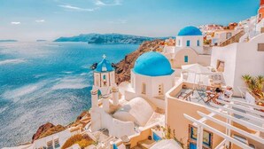 Um edifício costeiro com paredes brancas e cúpulas azuis, com vista para o mar.