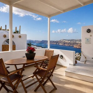 Eine Terrasse mit Tisch und Stühlen, einem Blumentopf und Blick auf eine Küstenlandschaft.