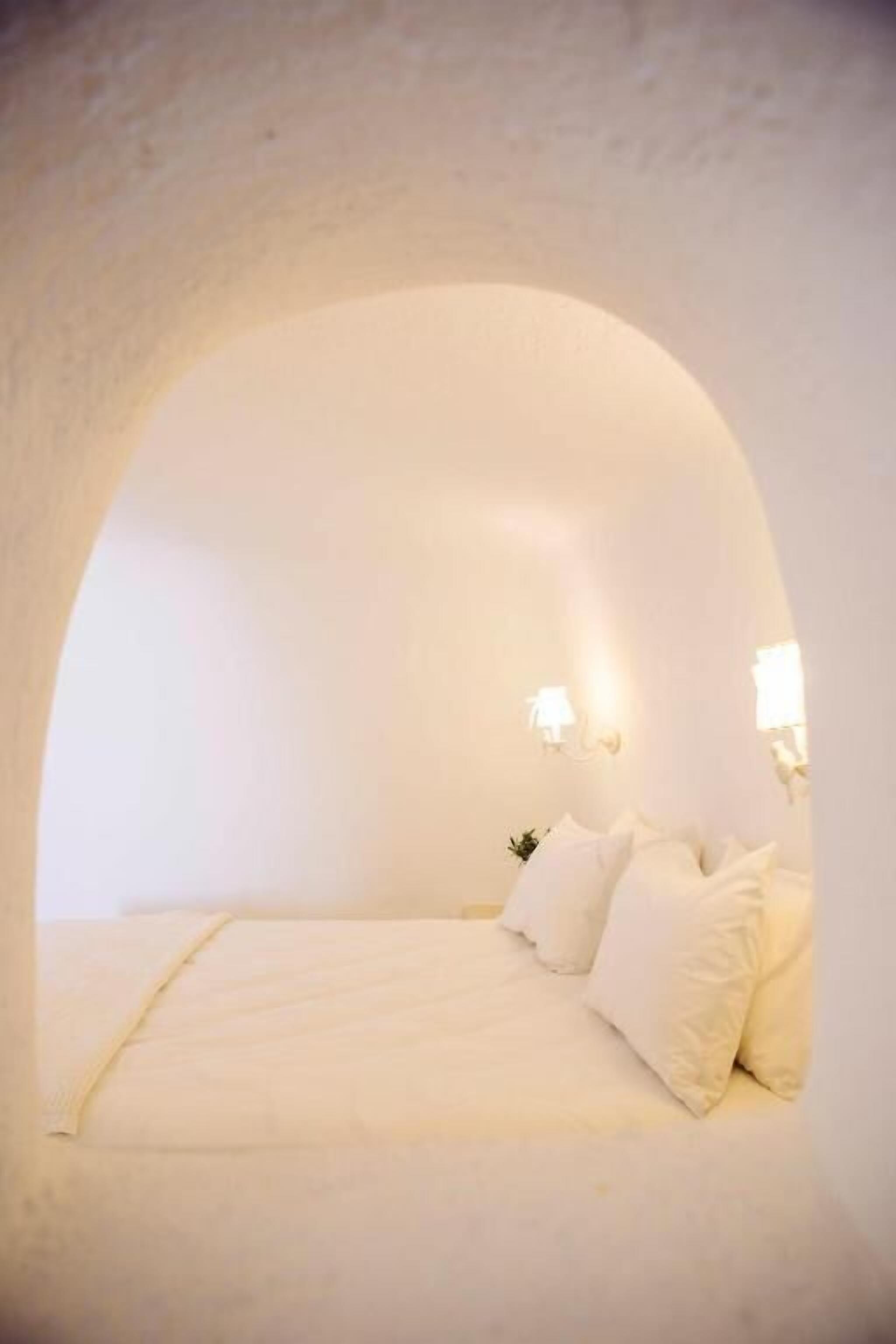 Un dormitorio acogedor de forma arqueada, con cama, almohadas e iluminación montada en la pared.
