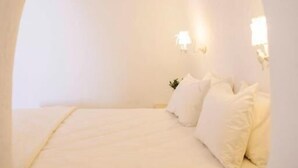 Quarto aconchegante com arco, cama, almofadas e iluminação na parede.