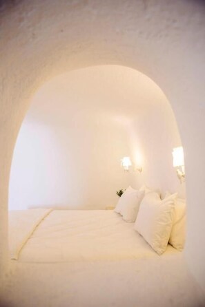 Ein gemütliches, bogenförmiges Schlafzimmer mit Bett, Kissen und Wandleuchten.
