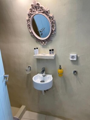 Ein Badezimmer mit einem weißen Waschbecken, einem Spiegel mit aufwändigem Rahmen und einem Ablagebereich mit Pflegeprodukten.