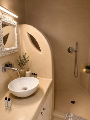 Een badkamer met een witte wastafel, een spiegel, een douche en een plant.