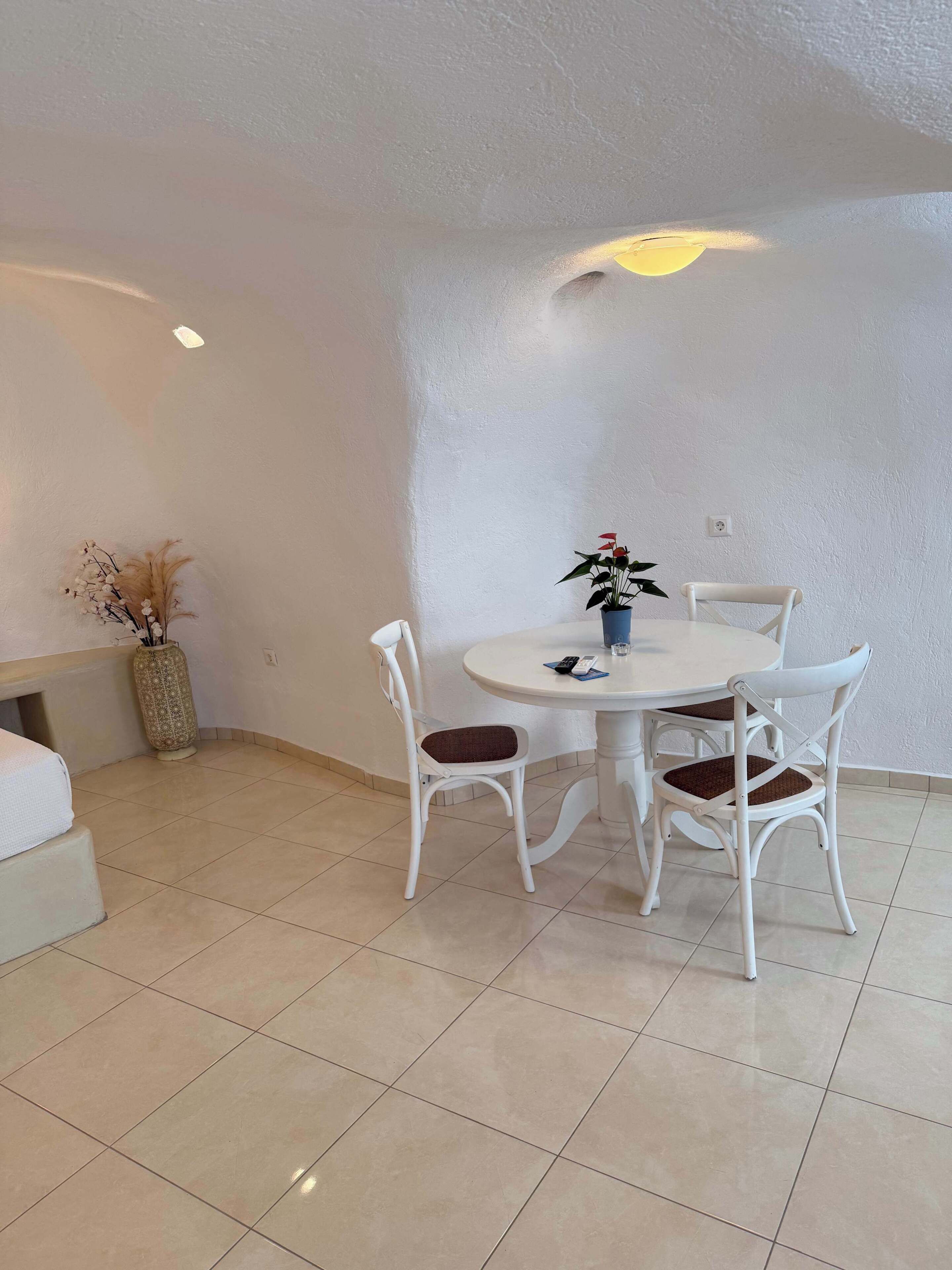 Un coin repas avec une table ronde et quatre chaises, un vase rempli de fleurs et un mur à texture.