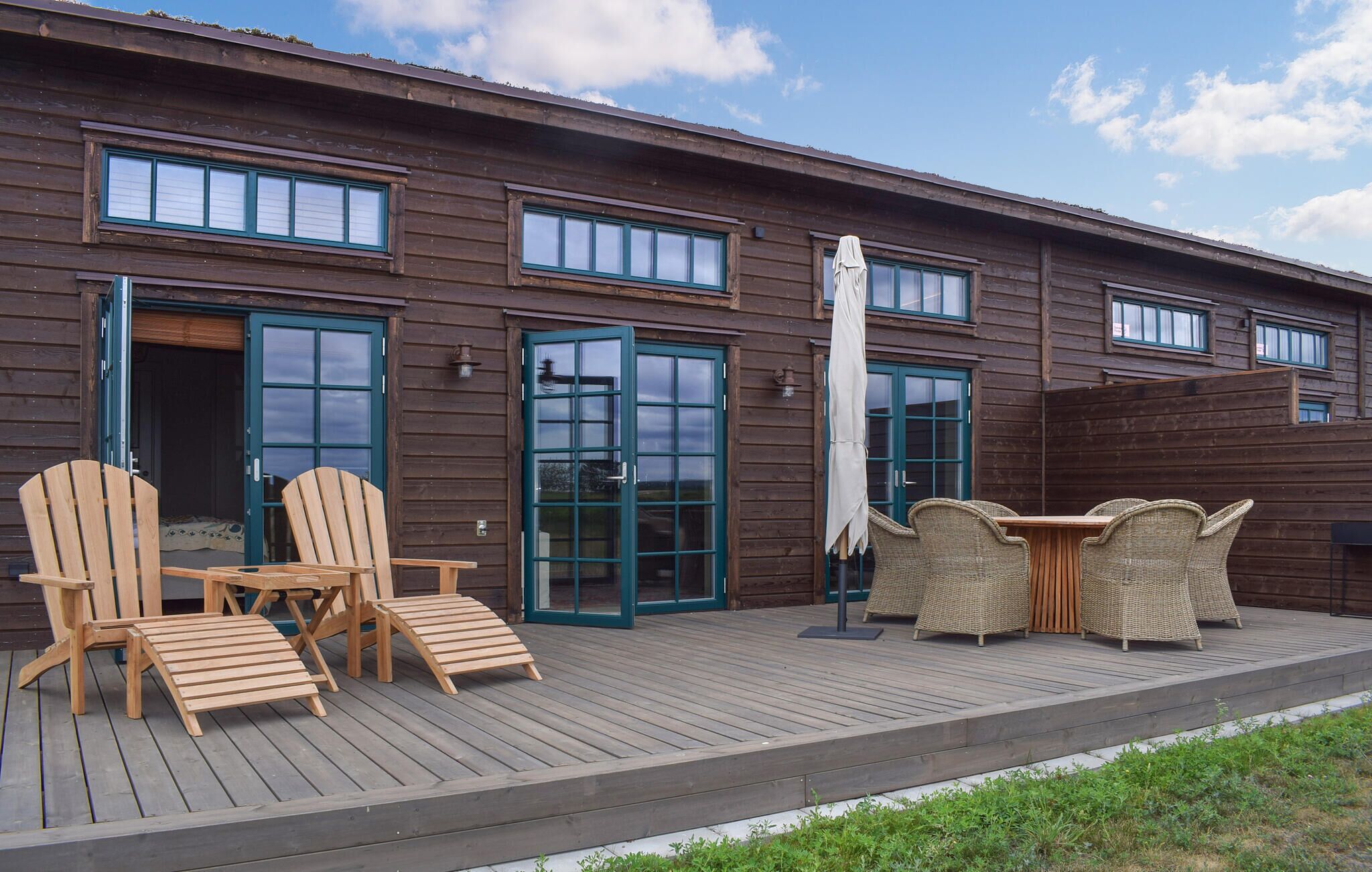 A wooden building with a deck, two wooden chairs, a table, and a covered umbrella.