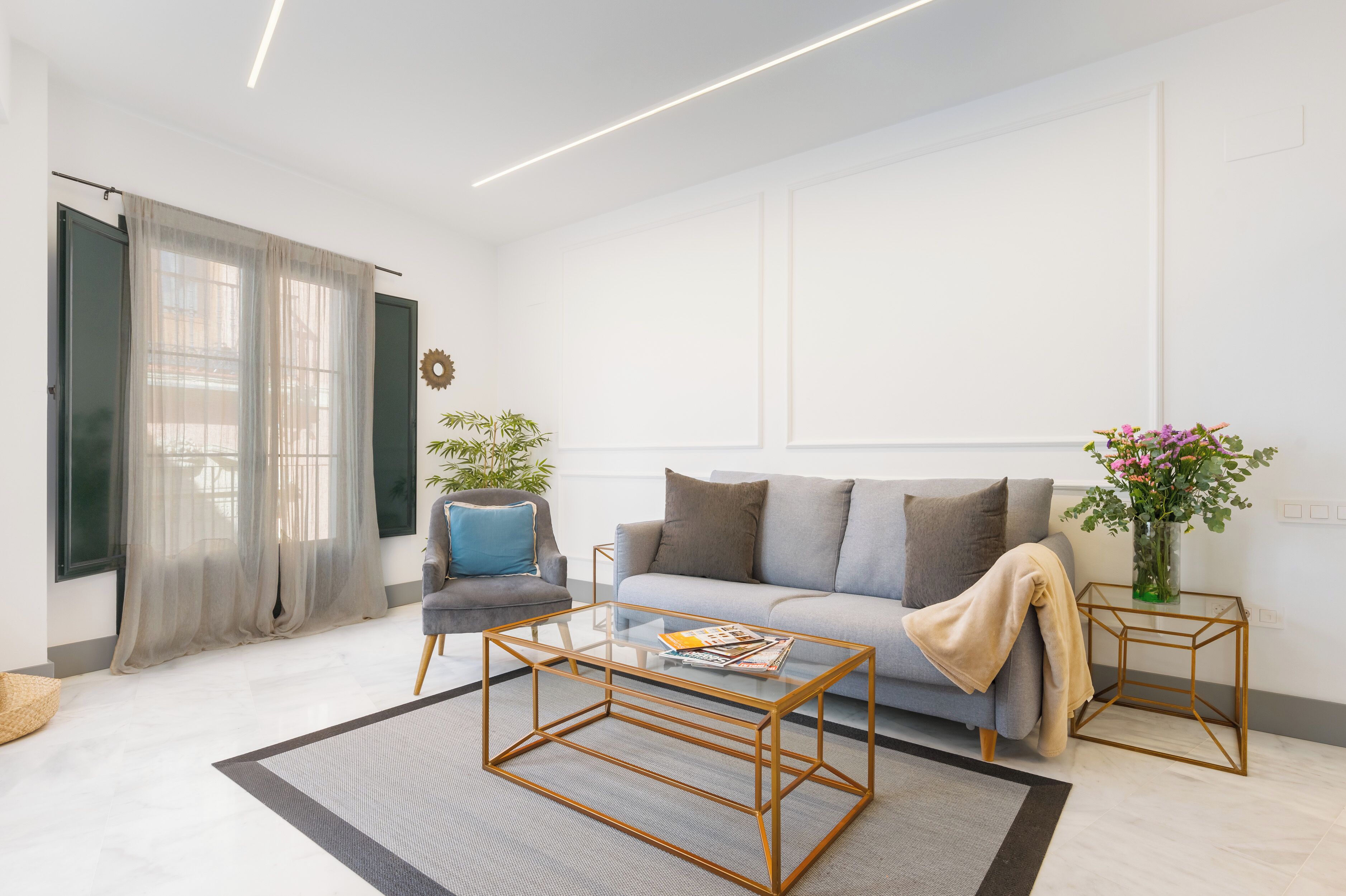 A modern living room with a sofa, two armchairs, a coffee table, a potted plant, and a vase with flowers.