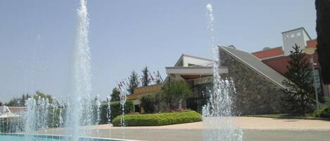 A pool with multiple fountains and a building in the background.