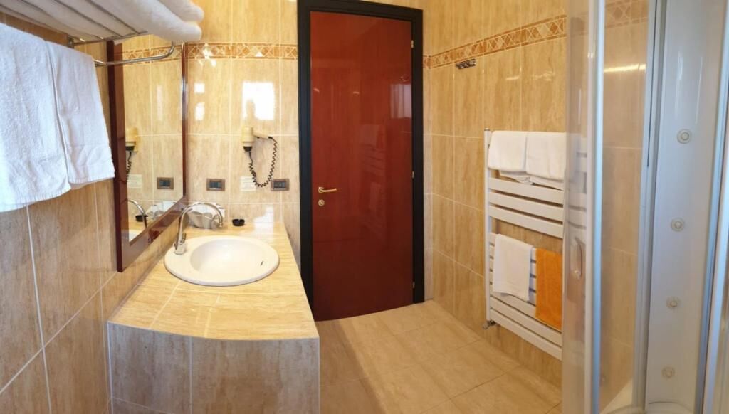 Ein Badezimmer mit Waschbecken, Spiegel, Handtuchhalter und Duschbereich.