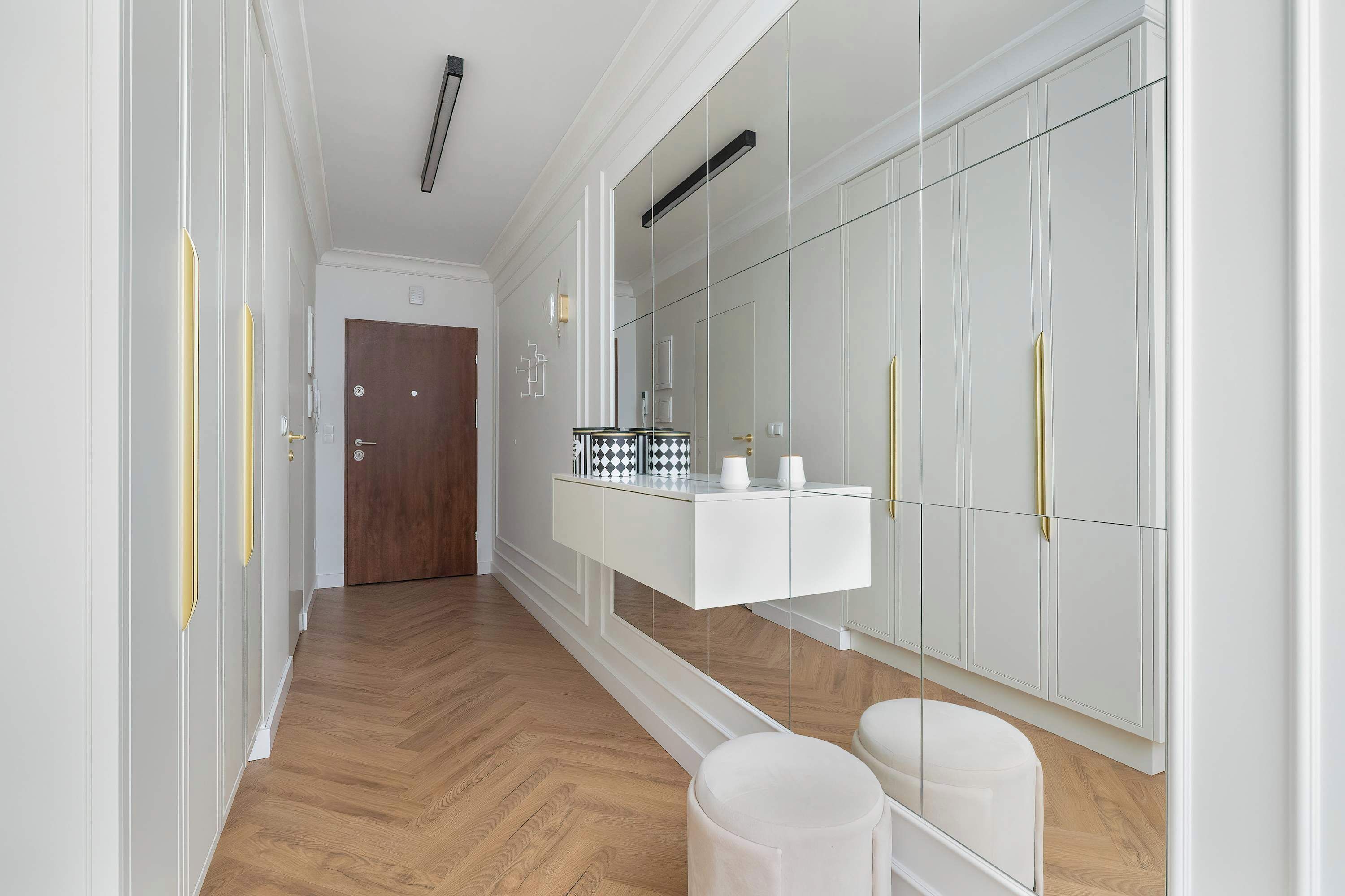 Un couloir avec un plancher en bois, une coiffeuse blanche avec un miroir et une armoire dont les poignées sont dorées.