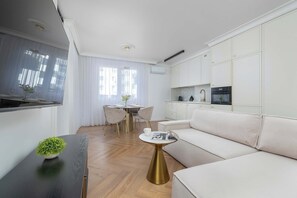 Una sala de estar moderna con un sofá, una mesa de comedor con sillas, una pequeña mesa de centro y un televisor montado en la pared.