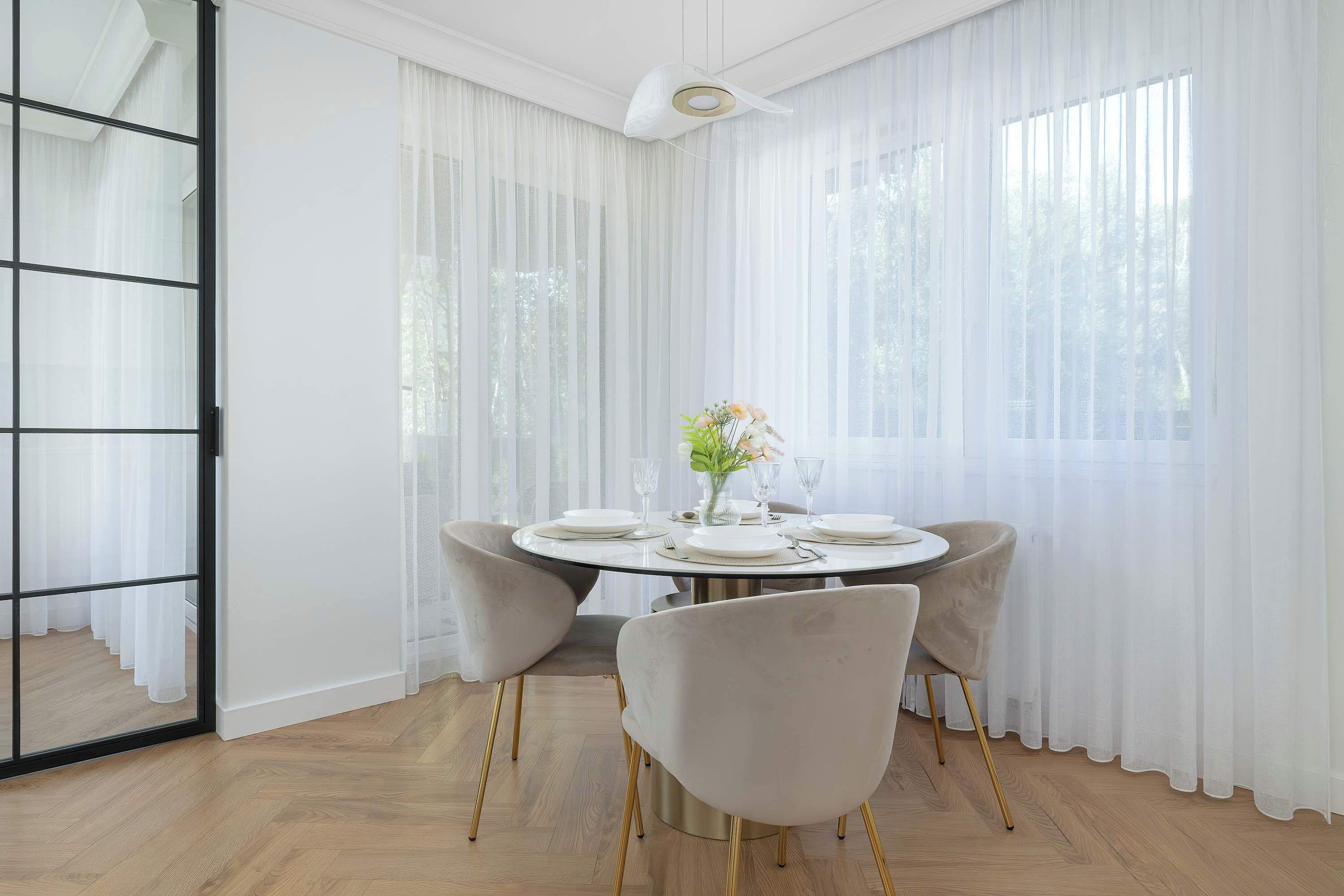 Un coin repas avec une table ronde dressée pour quatre personnes, deux chaises et un vase rempli de fleurs.