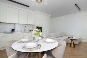 Una cocina moderna con armarios blancos, encimera de mármol y comedor con una mesa redonda para cuatro.