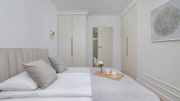 Quarto de hotel com cama, mesa de cabeceira com um vaso e chávenas, e um quadro abstrato grande na parede.