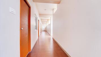 Un largo pasillo estrecho con puertas de madera a un lado y ventanas al otro, que conduce a una habitación luminosa al final.