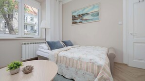 Ein Schlafzimmer mit einem Bett, einem Bild, einer Heizung, einem Fenster und einem Tisch mit einer Pflanze.