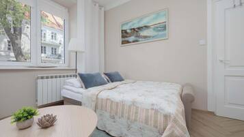 Ein Schlafzimmer mit einem Bett, einem Bild, einer Heizung, einem Fenster und einem Tisch mit einer Pflanze.