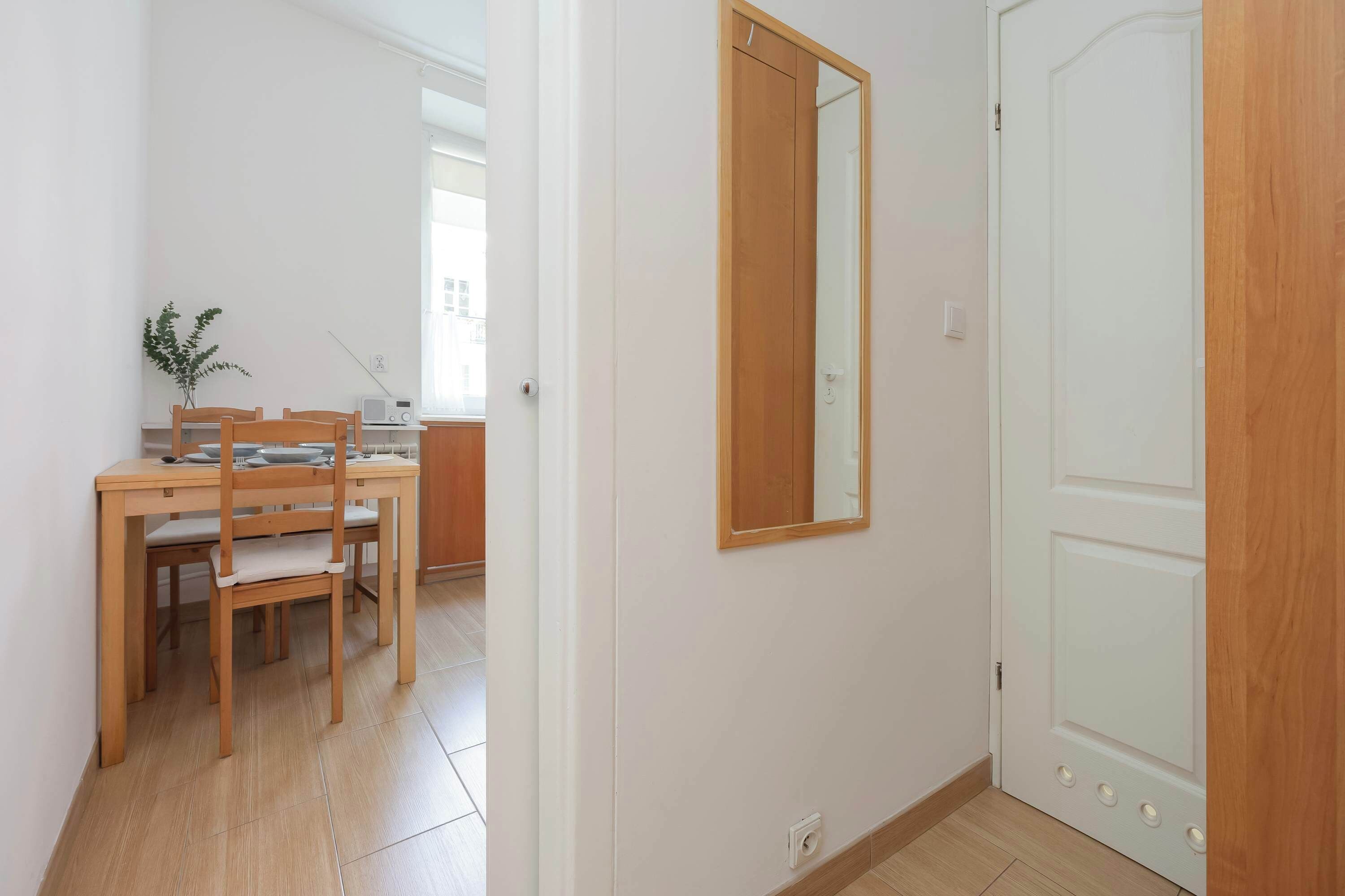 A room with a wooden dining table, chairs, a small plant, and a mirror on the wall.
