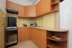 A compact kitchen with wooden cabinets, a stove, and a small countertop. - Cozy Studio with a Workspace | Near the Metro (Warszawa)