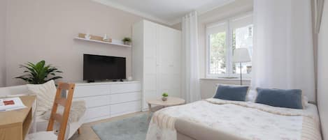 A bedroom with a bed, a desk, a chair, a television, a wardrobe, and a window.