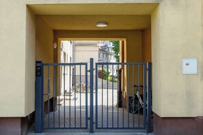 A gated entrance to a building with a metal gate, a bicycle parked outside, and a clear view of the street and buildings in the background. - Cozy Studio with a Workspace | Near the Metro (Warszawa)