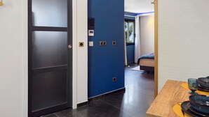 Habitación de hotel moderna con una puerta oscura, un muro azul decorativo, una cama y una mesa con platos y vasos.