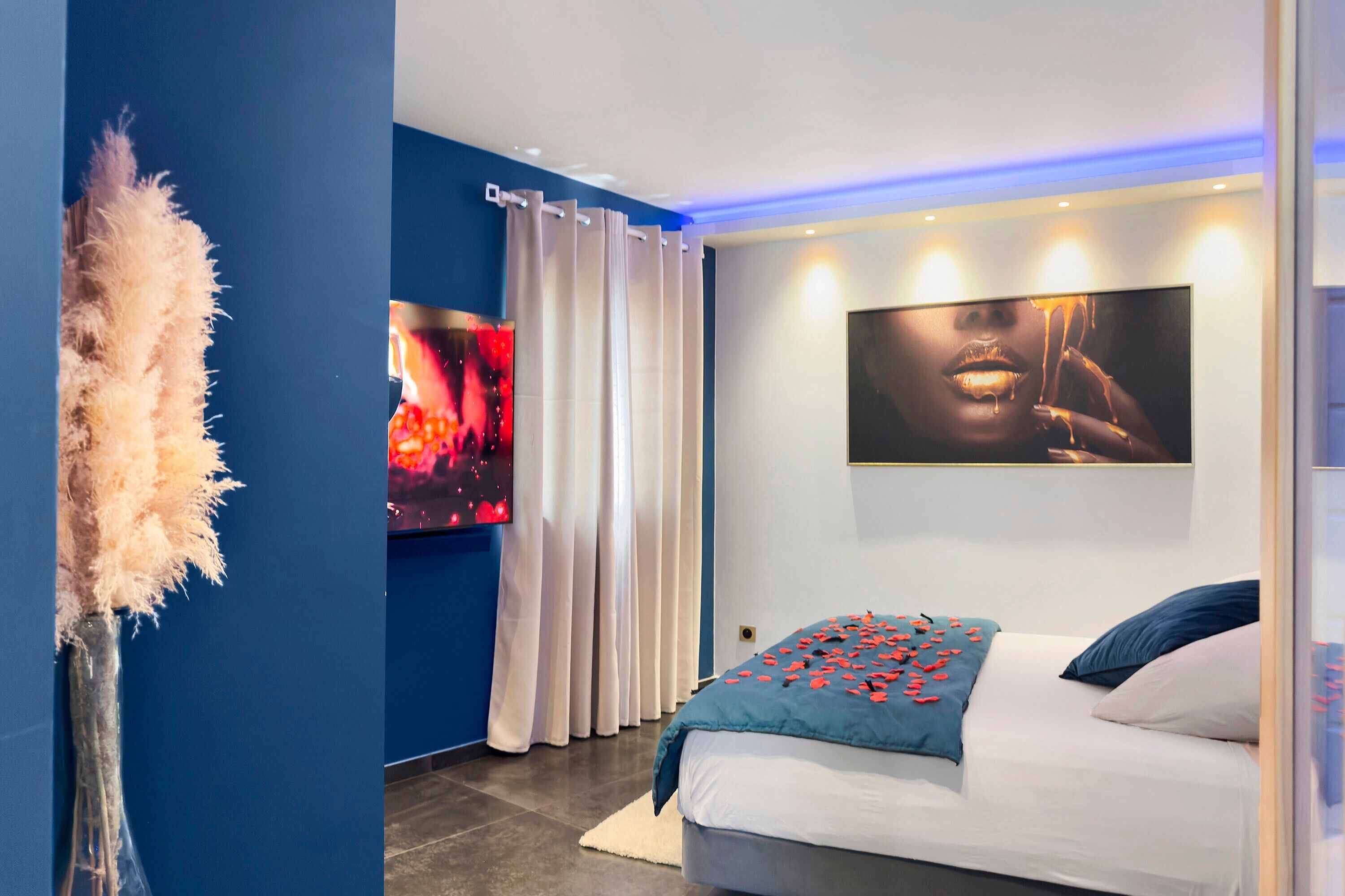 Une chambre moderne avec un lit, un téléviseur fixé au mur et un grand tableau abstrait.