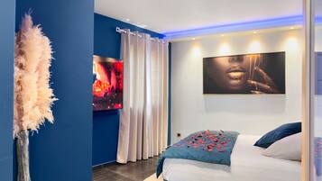 Une chambre moderne avec un lit, un téléviseur fixé au mur et un grand tableau abstrait.