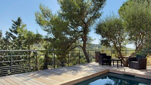 Un área junto a la piscina con terraza de madera, baranda metálica y mobiliario exterior.