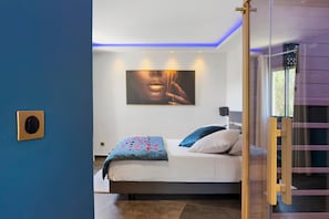 Una camera da letto con un letto, cuscini, un'opera d'arte appesa al muro e una porta che conduce a un'altra stanza.