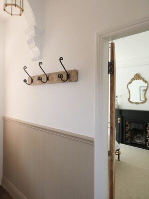 A hallway with a wooden wall-mounted shelf with three hooks, a white wall, and a door leading to another room. - The Farlan | Near North Shields Fish Quay (North Shields)