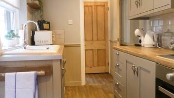 A kitchen with wooden flooring, a sink, cabinets, and a door leading to another room.