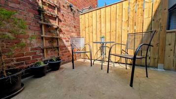A patio area with a brick wall, wooden fence, metal chairs, and potted plants.
