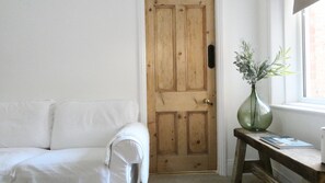 A room with a wooden door, a white sofa, and a small table with a vase.