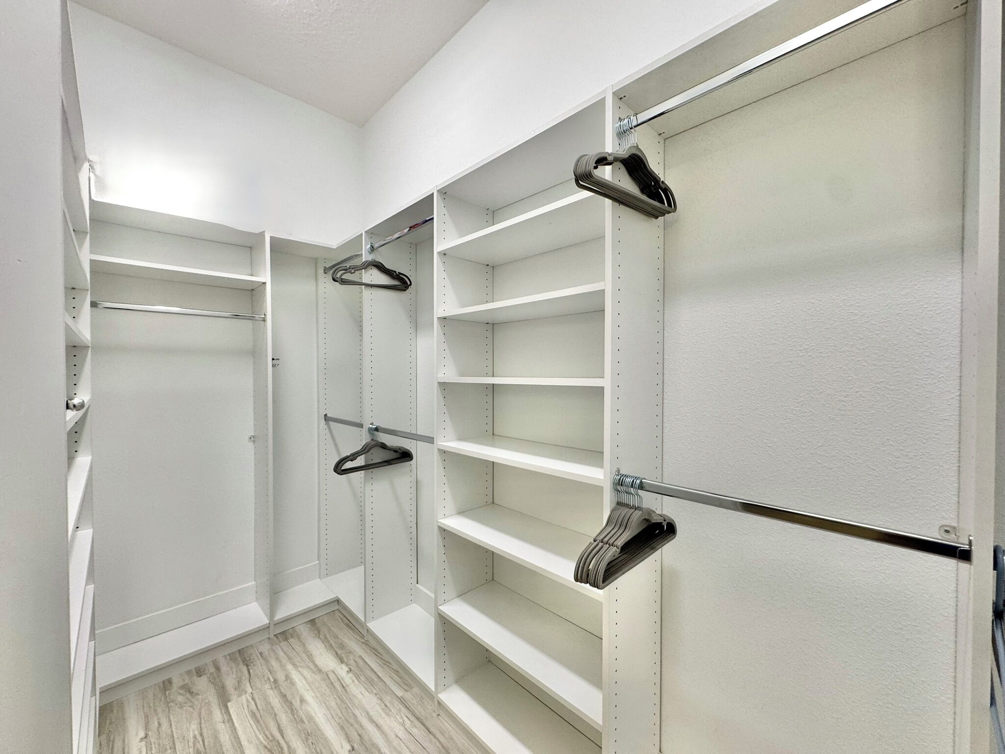 Un dressing accessible sans porte, doté d’étagères ouvertes, de cintres en métal et d’une porte de placard miroir.