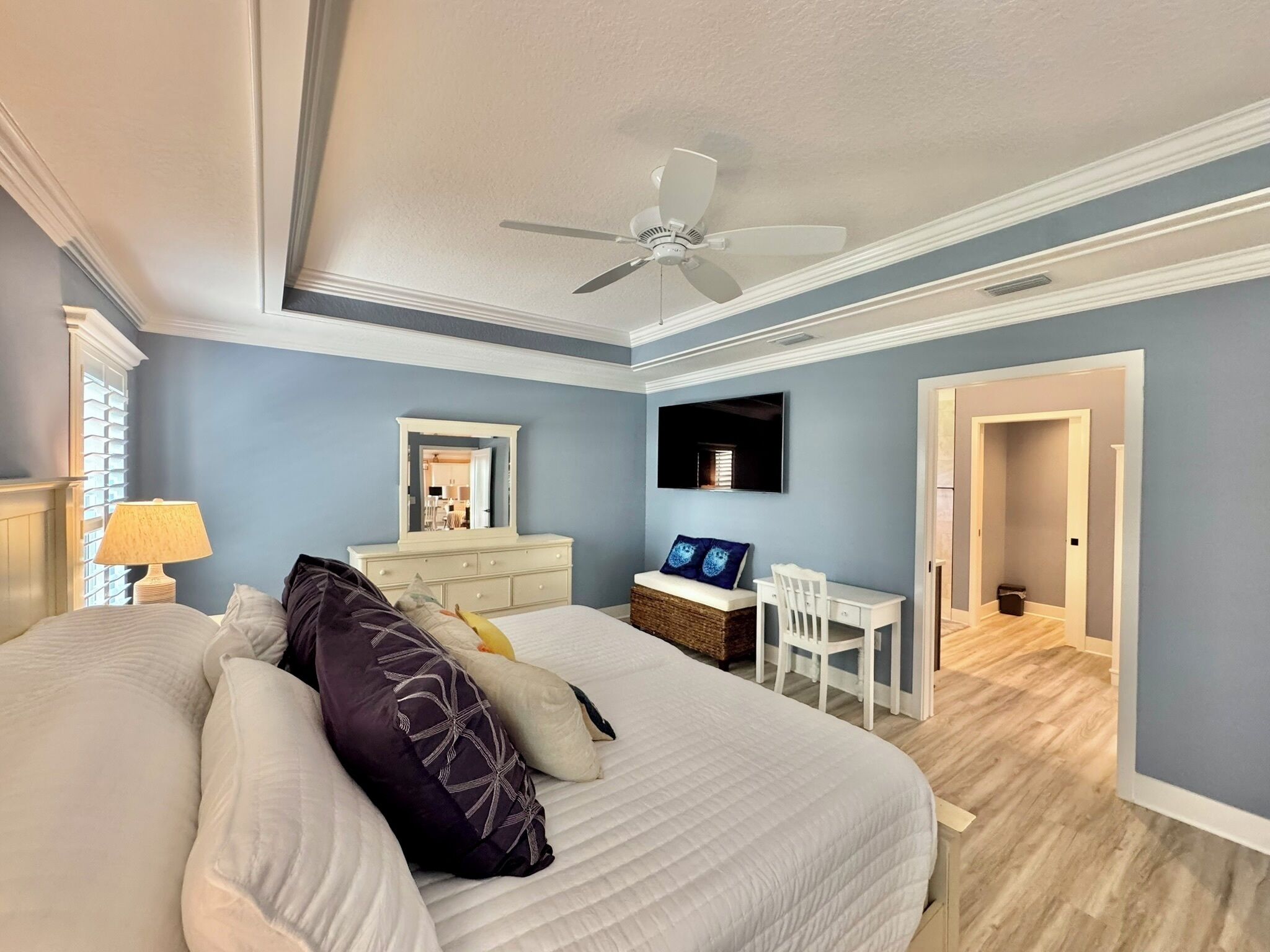 A bedroom with a large bed, a desk, a chair, a television, and a ceiling fan.