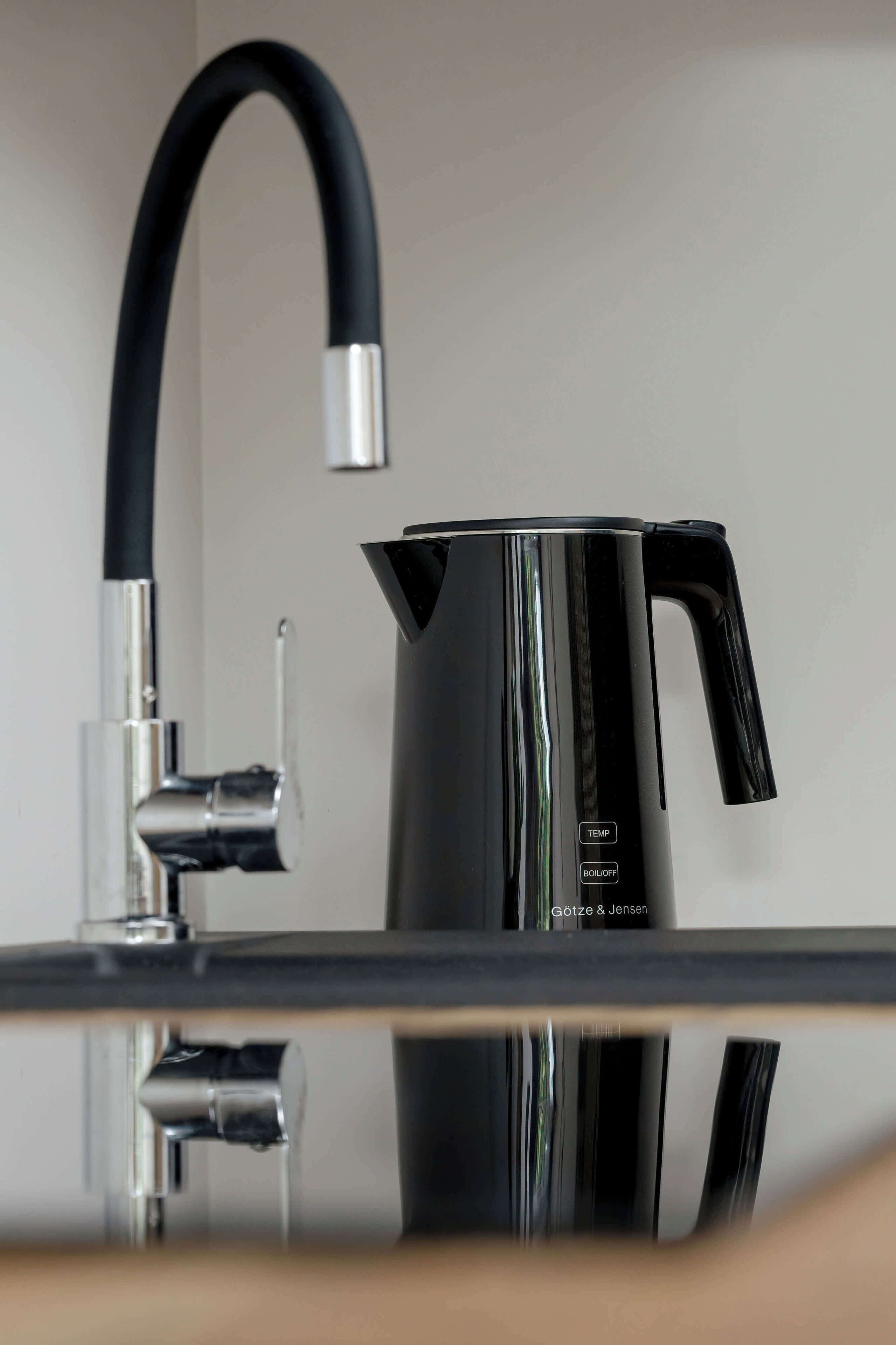 Une cuisine moderne avec une bouilloire noire au design épuré et un robinet aux lignes courbes.