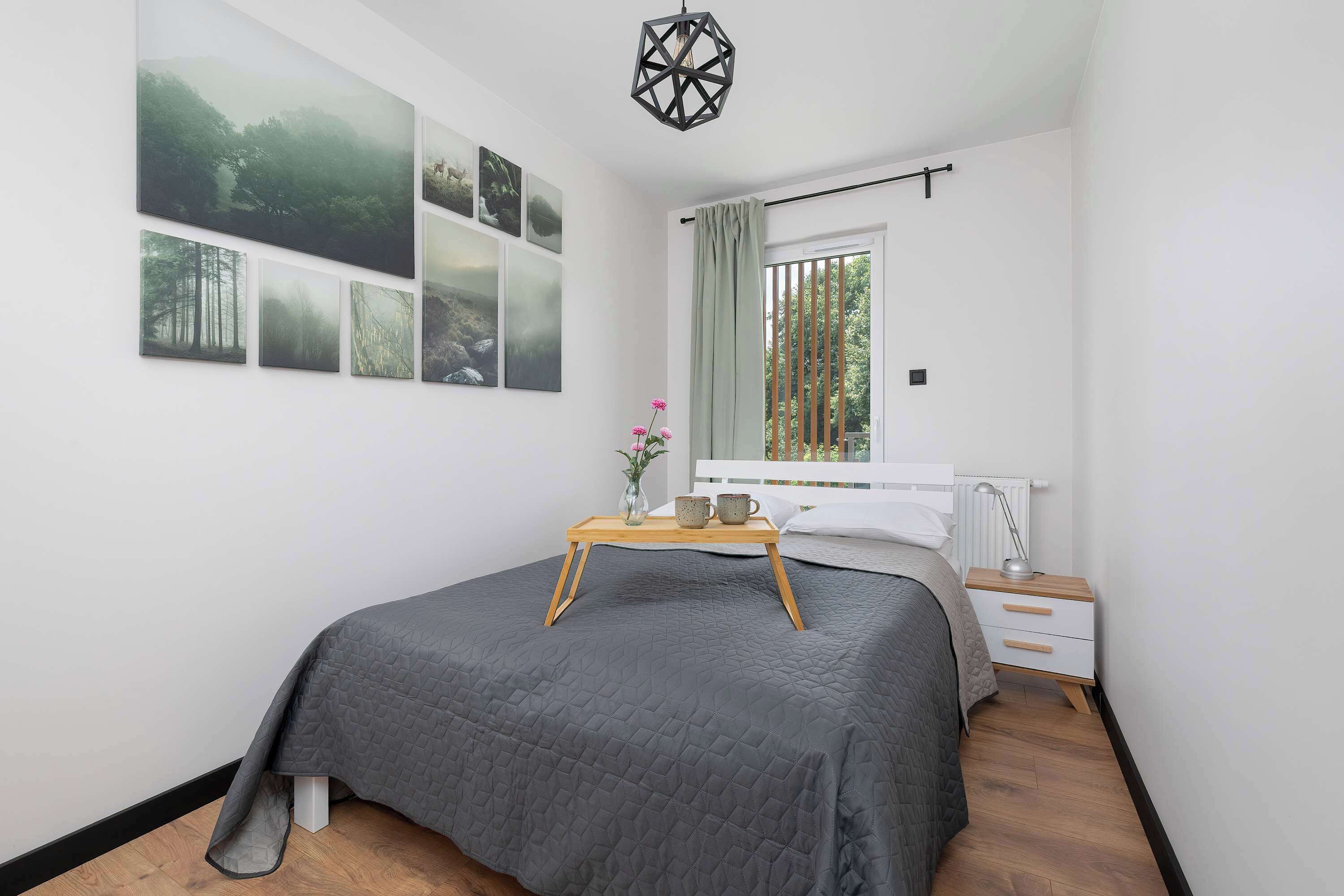 Une chambre à coucher avec un lit, une table de chevet avec une lampe, une fenêtre avec des rideaux et des œuvres d’art murales.
