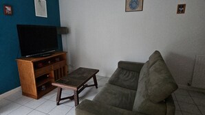 A living room with a sofa, a television on a wooden stand, and a woven ceiling light fixture. - L'amirauté pour 4 personnes (La Rochelle)