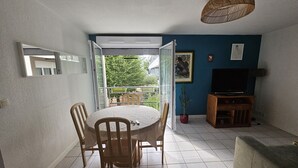 A dining area with a round table and chairs, a television, a sofa, and a potted plant. - L'amirauté pour 4 personnes (La Rochelle)