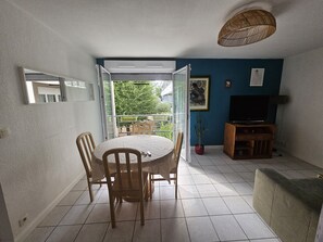 Ein Essbereich mit rundem Tisch und Stühlen, einem Fernseher, einer Couch und einem Topf mit Pflanze.