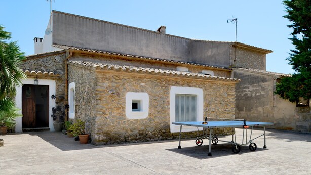 A stone building with a tiled roof, a door, and a small window. There is a table with a table tennis table and a cart. - Hillside Villa With Pool for 5 (Pollença)