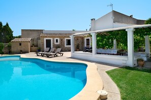 A swimming pool with lounge chairs, a covered patio area, and a stone building with a tiled roof. - Hillside Villa With Pool for 5 (Pollença)
